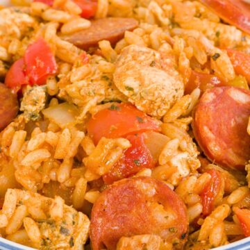 One pot Southern chicken and sausage rice served in a white bowl with blue stripes, featuring sliced smoked sausage, tender seasoned chicken chunks, rice, diced tomatoes, onions, and bell peppers in a rich tomato based sauce. Hearty comfort food dinner with bold Southern flavors.