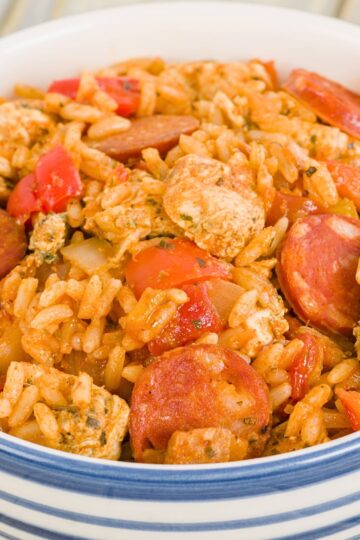 One pot Southern chicken and sausage rice served in a white bowl with blue stripes, featuring sliced smoked sausage, tender seasoned chicken chunks, rice, diced tomatoes, onions, and bell peppers in a rich tomato based sauce. Hearty comfort food dinner with bold Southern flavors.