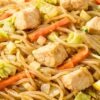 Close-up of Filipino pancit noodles with diced chicken, shredded cabbage, carrots, and onions tossed in a savory sauce. Thin rice noodles glisten in a white bowl, showing tender chicken pieces and crisp vegetables in this classic Filipino noodle stir fry.