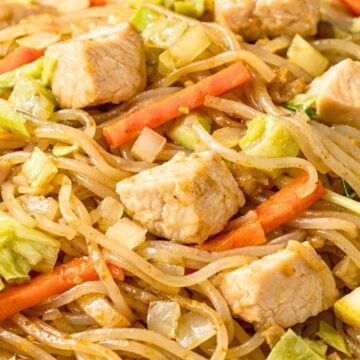 Close-up of Filipino pancit noodles with diced chicken, shredded cabbage, carrots, and onions tossed in a savory sauce. Thin rice noodles glisten in a white bowl, showing tender chicken pieces and crisp vegetables in this classic Filipino noodle stir fry.
