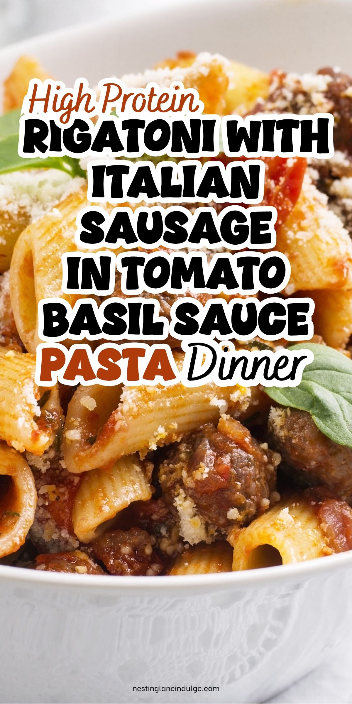 High protein rigatoni with Italian sausage in tomato basil sauce pasta dinner. Close-up of rigatoni pasta with sausage chunks, tomato sauce, grated Parmesan, and fresh basil in a white bowl. Text on image: &ldquo;High Protein Rigatoni With Italian Sausage in Tomato Basil Sauce Pasta Dinner&rdquo; and &ldquo;nestinglaneindulge.com&rdquo;.